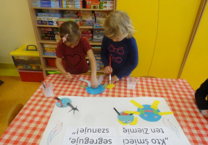 Dwie dziewczynki dekorują plakat ekologiczny, naklejają elementy z kolorowego papieru.